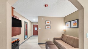 Un pasillo con un sofá, un televisor, cuadros enmarcados en la pared y una puerta al fondo.