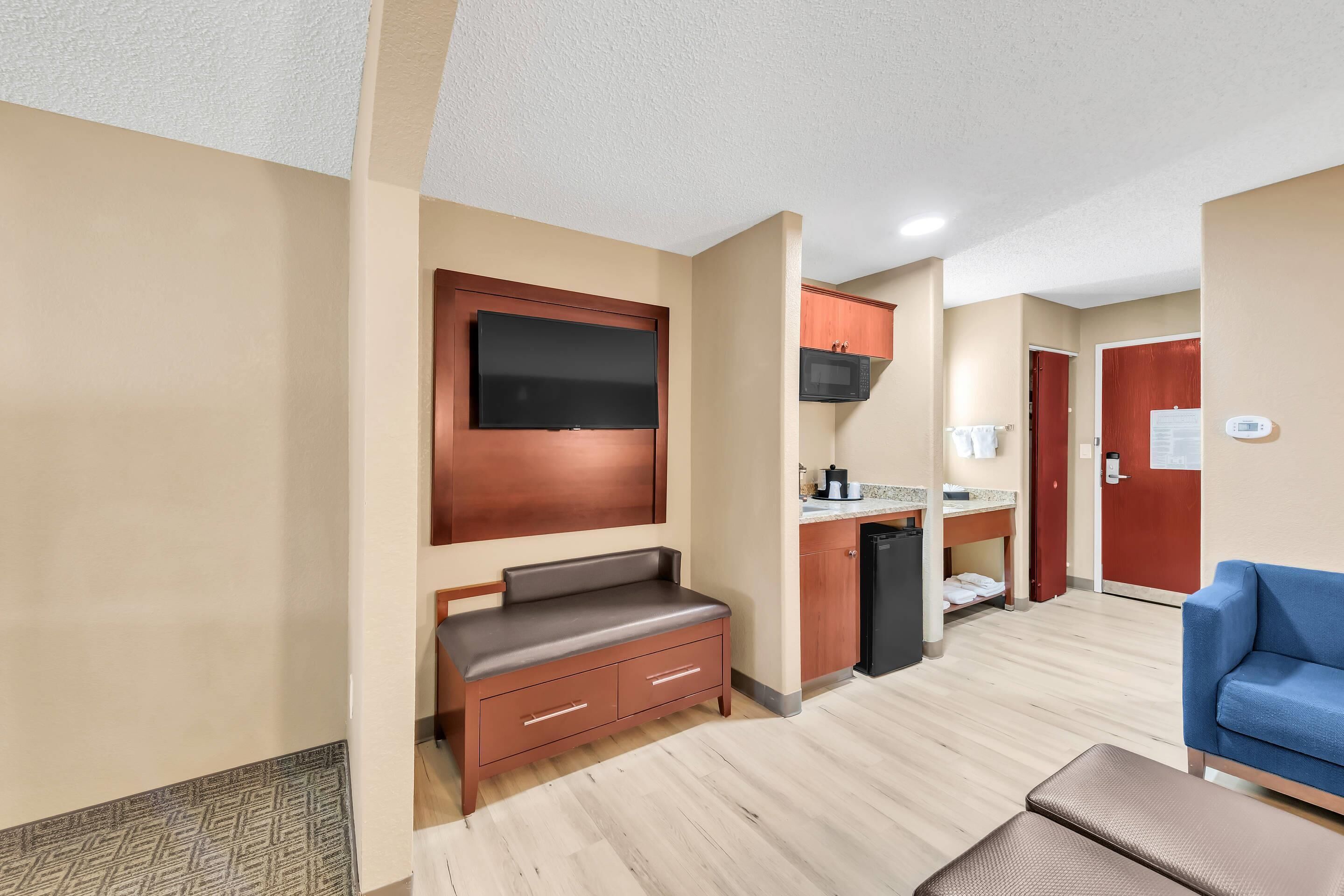 A hotel room with a kitchenette, a seating area with a bench, and a blue sofa.