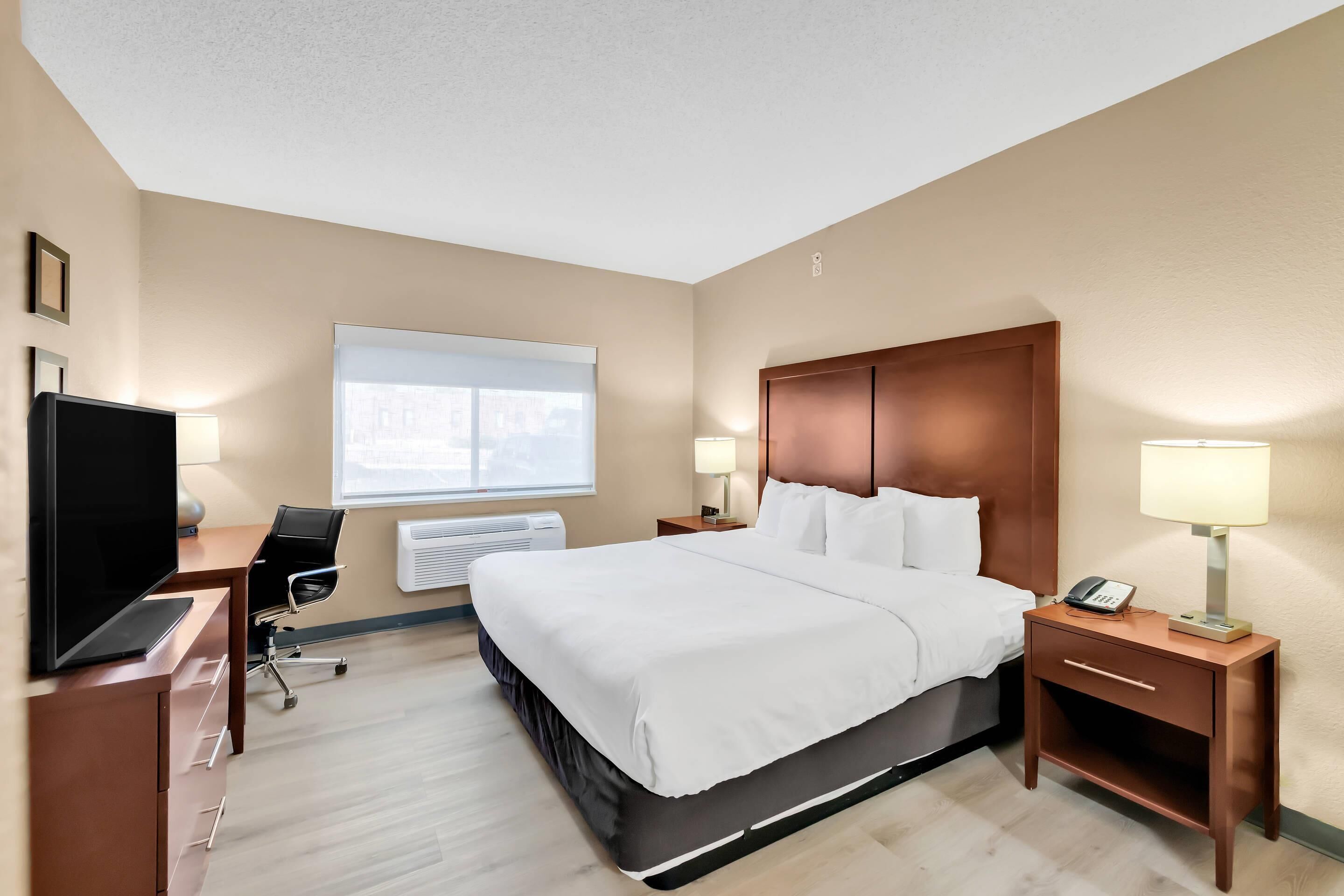 Habitación de hotel con cama, mesita de noche, lámpara, escritorio con computadora y televisor.