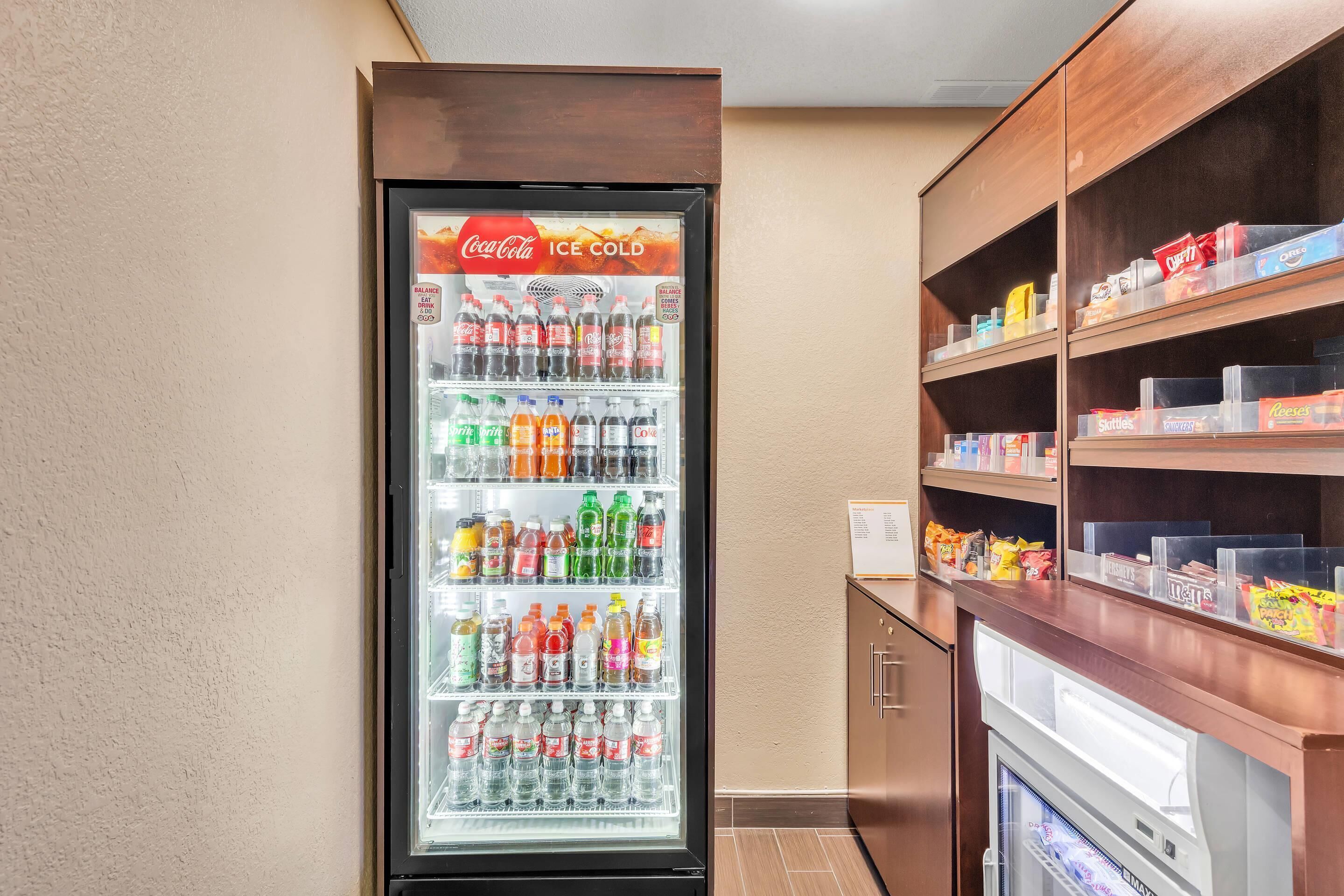 A Coca-Cola refrigerator stocked with various beverages, a snack bar with assorted snacks, and a small freezer unit.