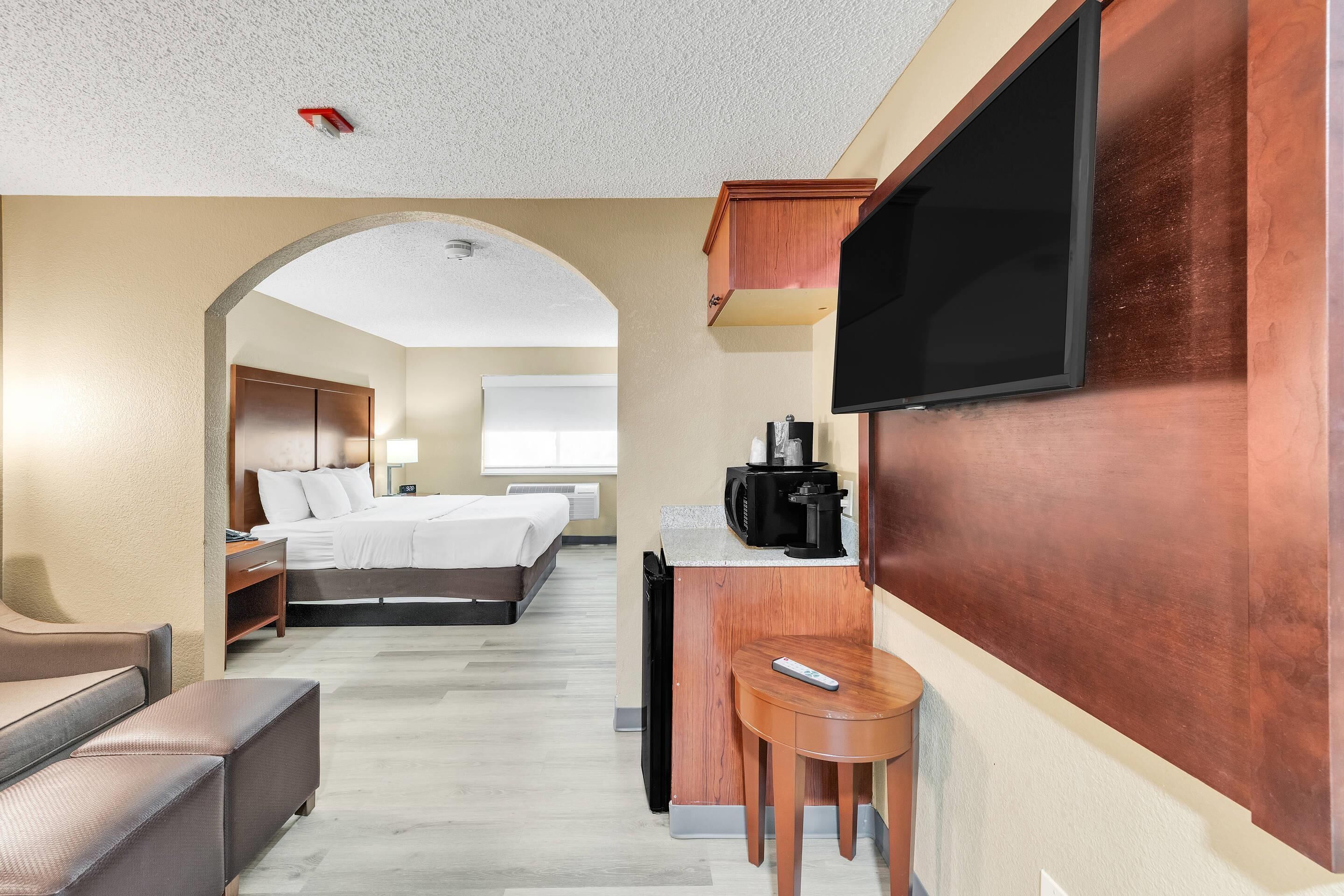 A hotel room with a bed, a desk with a coffee maker, a TV, and a small seating area.