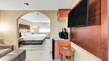 A hotel room with a bed, a desk with a coffee maker, a TV, and a small seating area.