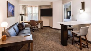 A hotel room with a sofa, a desk, a chair, a flat-screen TV, and a large window with curtains. - Residence Inn by Marriott Denver Southwest/Lakewood (Lakewood)