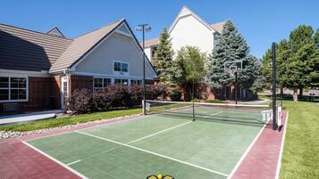 Una cancha de tenis al aire libre junto a edificios residenciales, con cielo despejado y entorno bien cuidado.