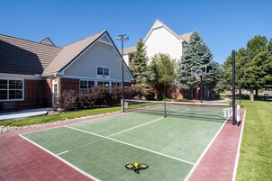 Una cancha de tenis al aire libre junto a edificios residenciales, con cielo despejado y entorno bien cuidado.