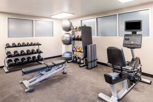 Un gimnasio con mancuernas, una banca, una máquina de remo y una bicicleta estática.