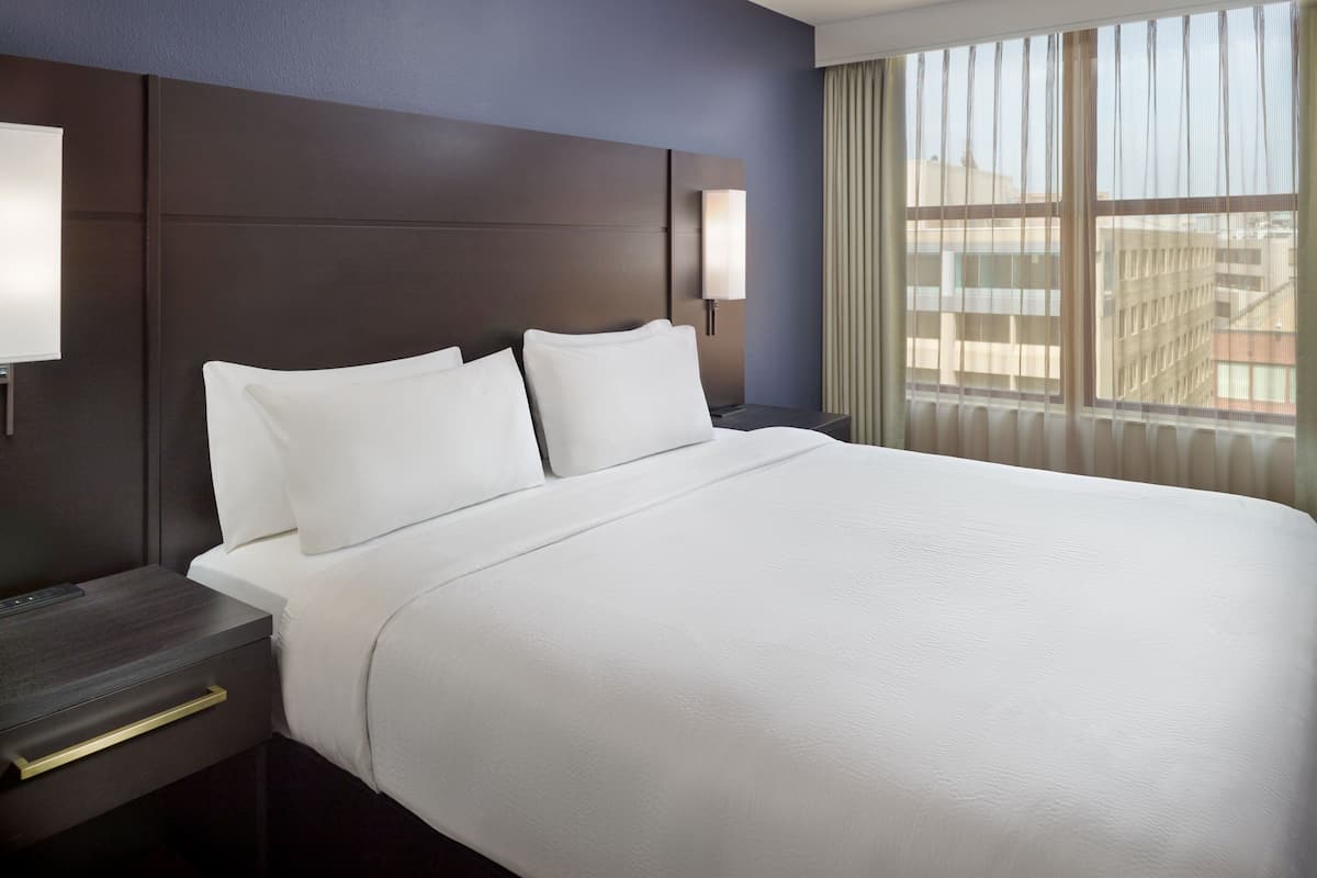 Une chambre d’hôtel avec un grand lit, une table de chevet avec une lampe et une fenêtre avec des rideaux.