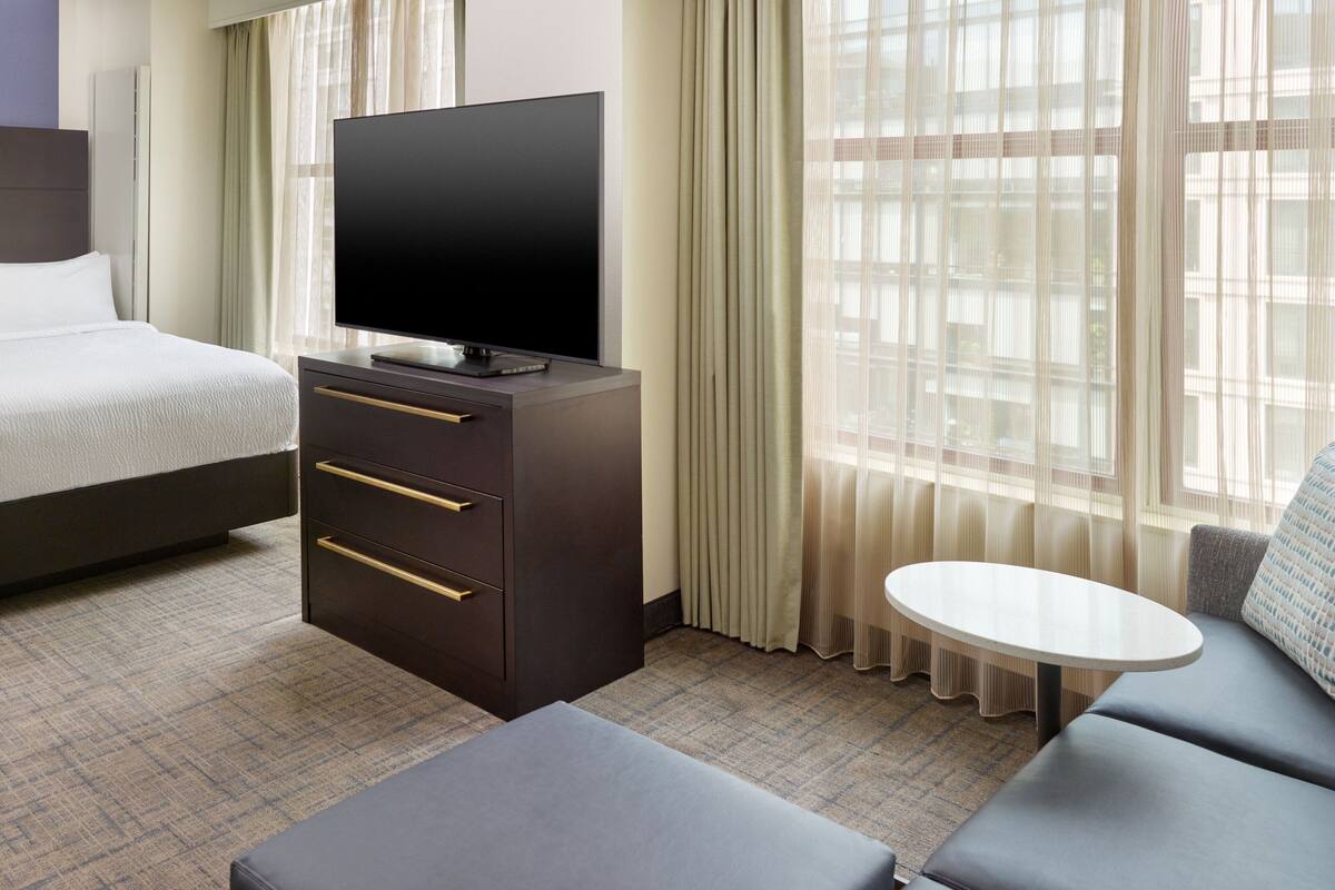 Une chambre d’hôtel avec un lit, un téléviseur posé sur une commode, un canapé et une petite table.