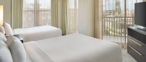 A hotel room with two beds, a TV, and a balcony with a city view.