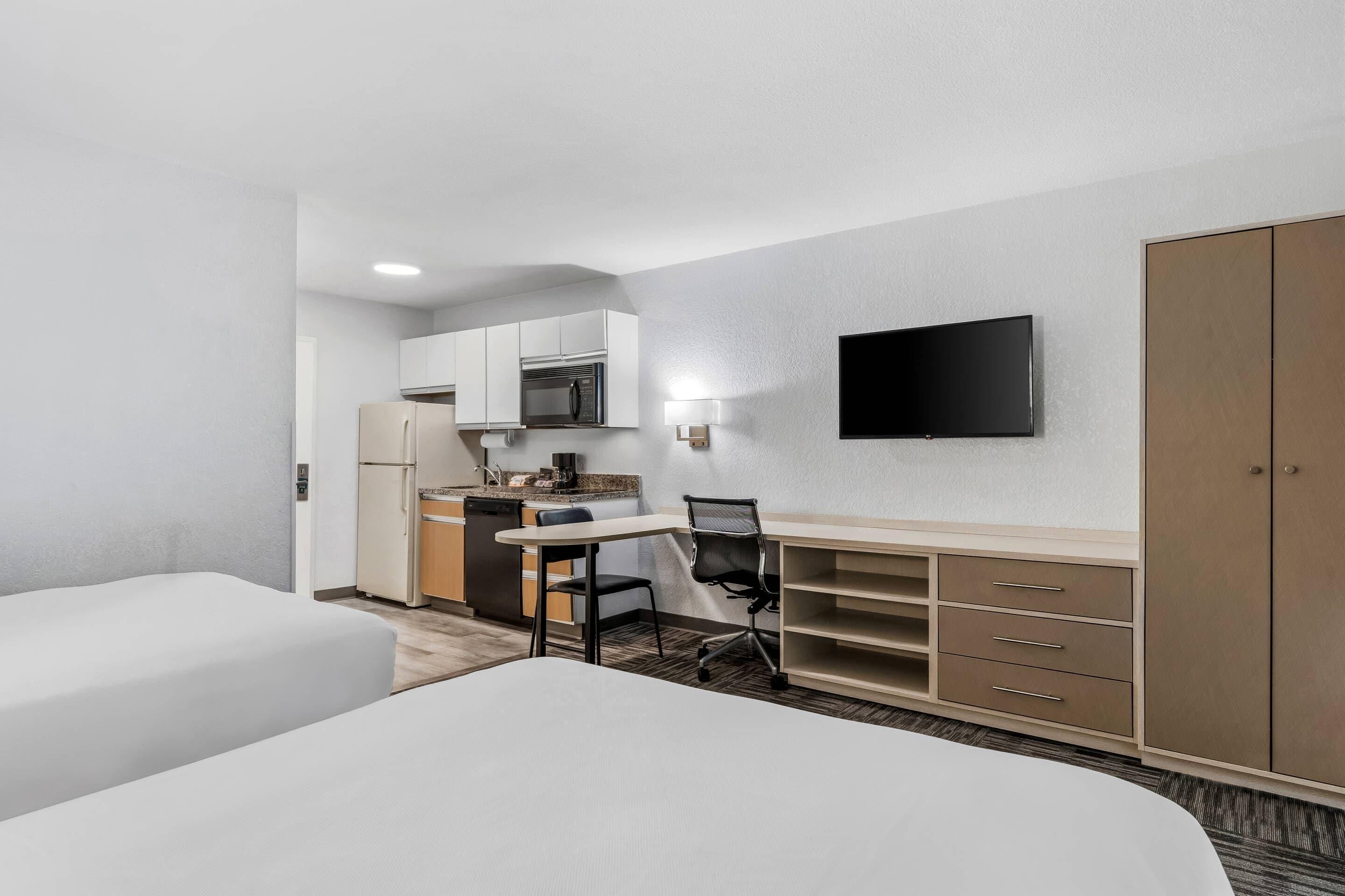 Habitación de hotel con cama, escritorio y silla, televisión, armario y kitchenette.