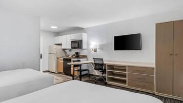 Habitación de hotel con cama, escritorio y silla, televisión, armario y kitchenette.