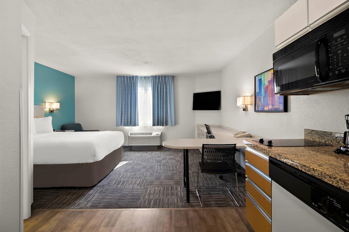 A hotel room with a bed, a desk, a microwave, a TV, and a painting on the wall.