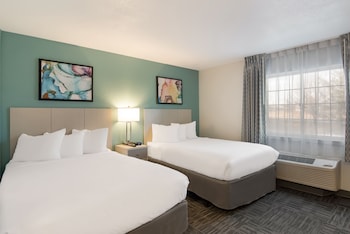 Two single beds with nightstands and lamps, set against a backdrop of abstract art and a large window. at MainStay Suites Orlando Altamonte Springs