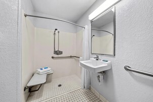 Un espacio de ducha pequeño y cerrado, con una barra de apoyo, un lavamanos blanco y un espejo.