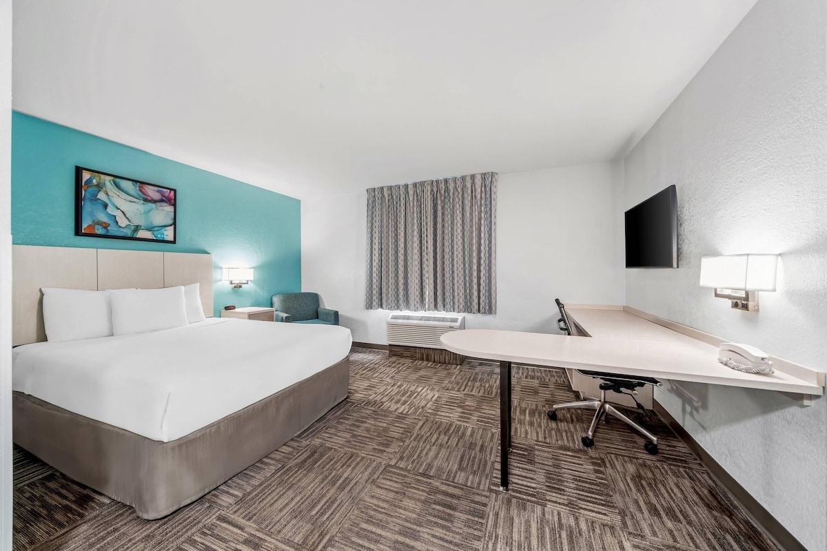 A hotel room with a bed, a desk, a chair, a television, and a window with curtains.