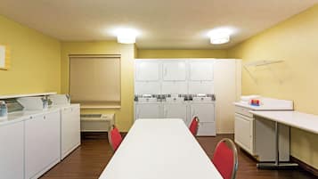 Una sala de lavandería con una mesa larga, sillas rojas y varias lavadoras.
