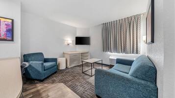A modern hotel room with a sofa, a chair, a small table, a TV, and a window with curtains.
