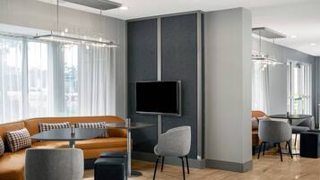 A modern hotel lobby with a sofa, chairs, a TV, and a dining area.