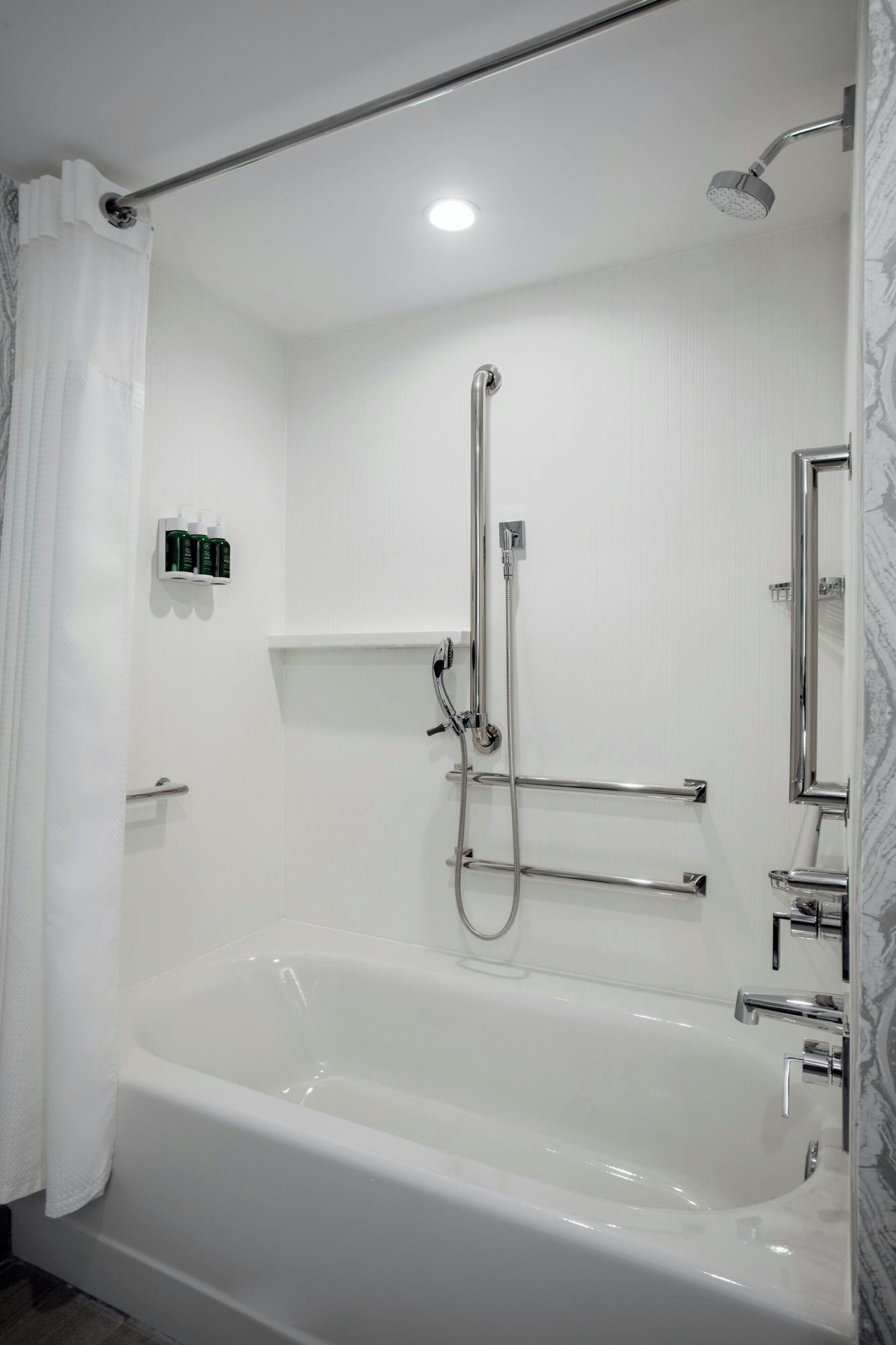 A modern bathroom with a white bathtub, a handheld showerhead, and a wall-mounted mirror.