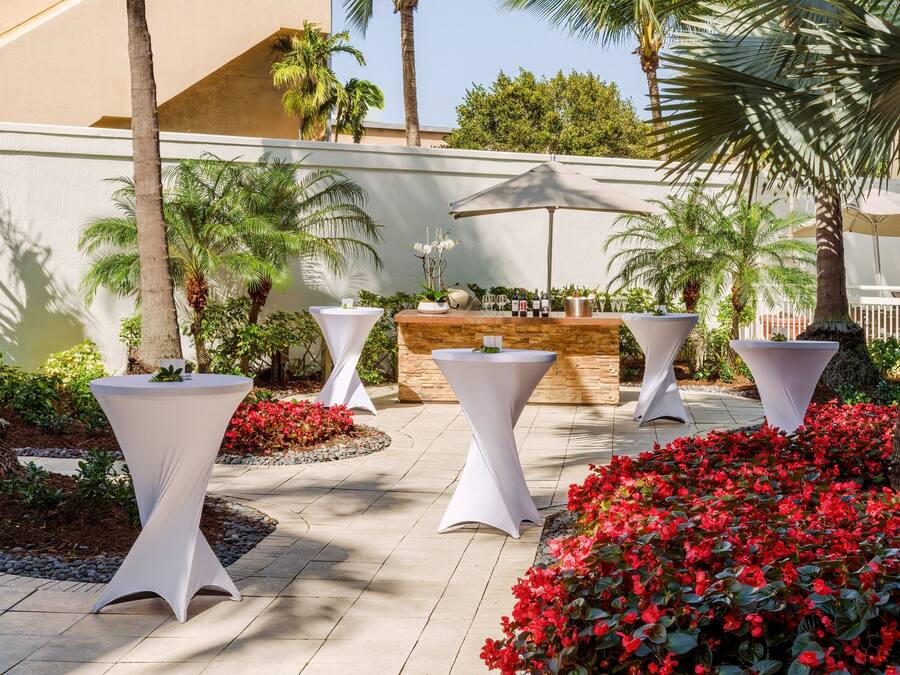 Un'area patio con tavoli bianchi, un bar e fiori rossi.