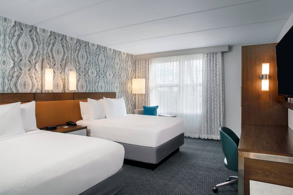 Quarto de hotel com duas camas, uma mesa, uma cadeira e uma televisão.