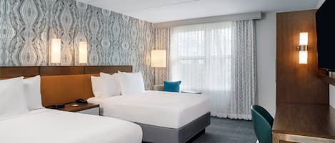 A hotel room with two beds, a desk, a chair, and a TV.