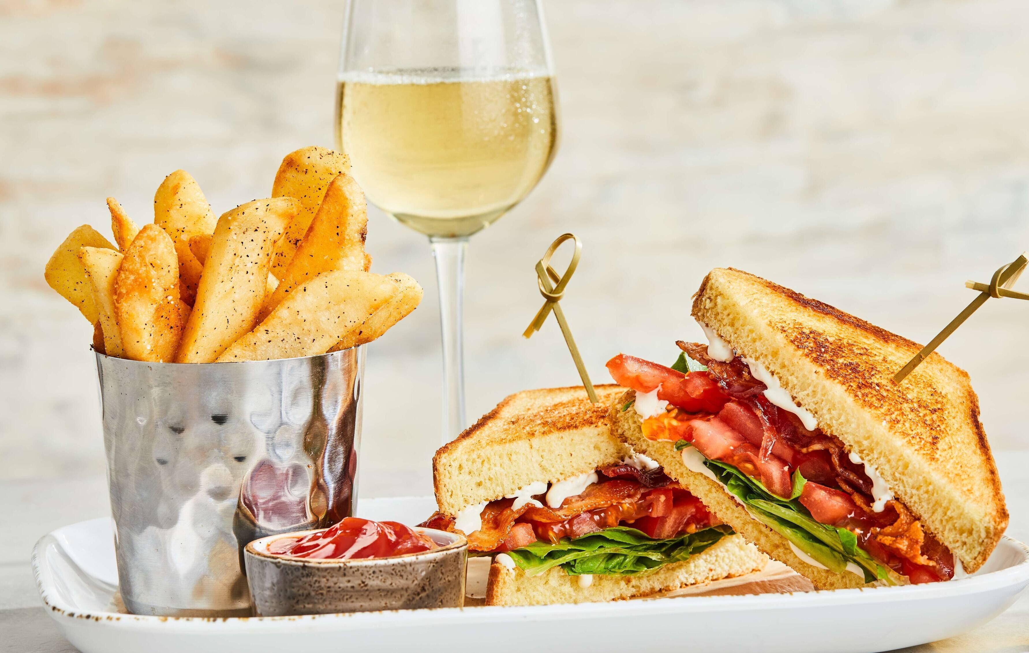Ein Sandwich mit Pommes und einem Glas Weißwein.