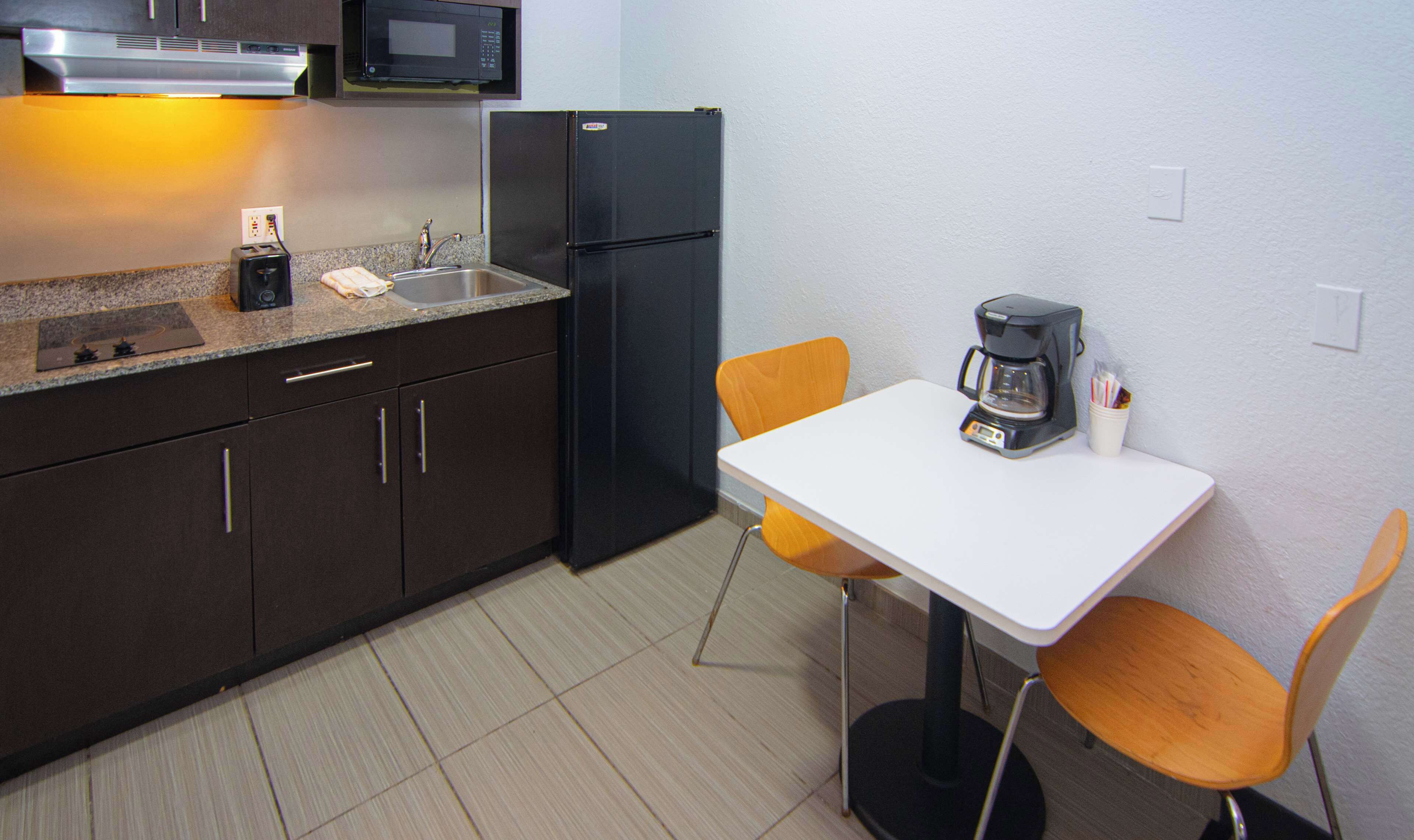 Una kitchenette compacta equipada con microondas, refrigerador, lavaplatos y una pequeña mesa con cafetera.
