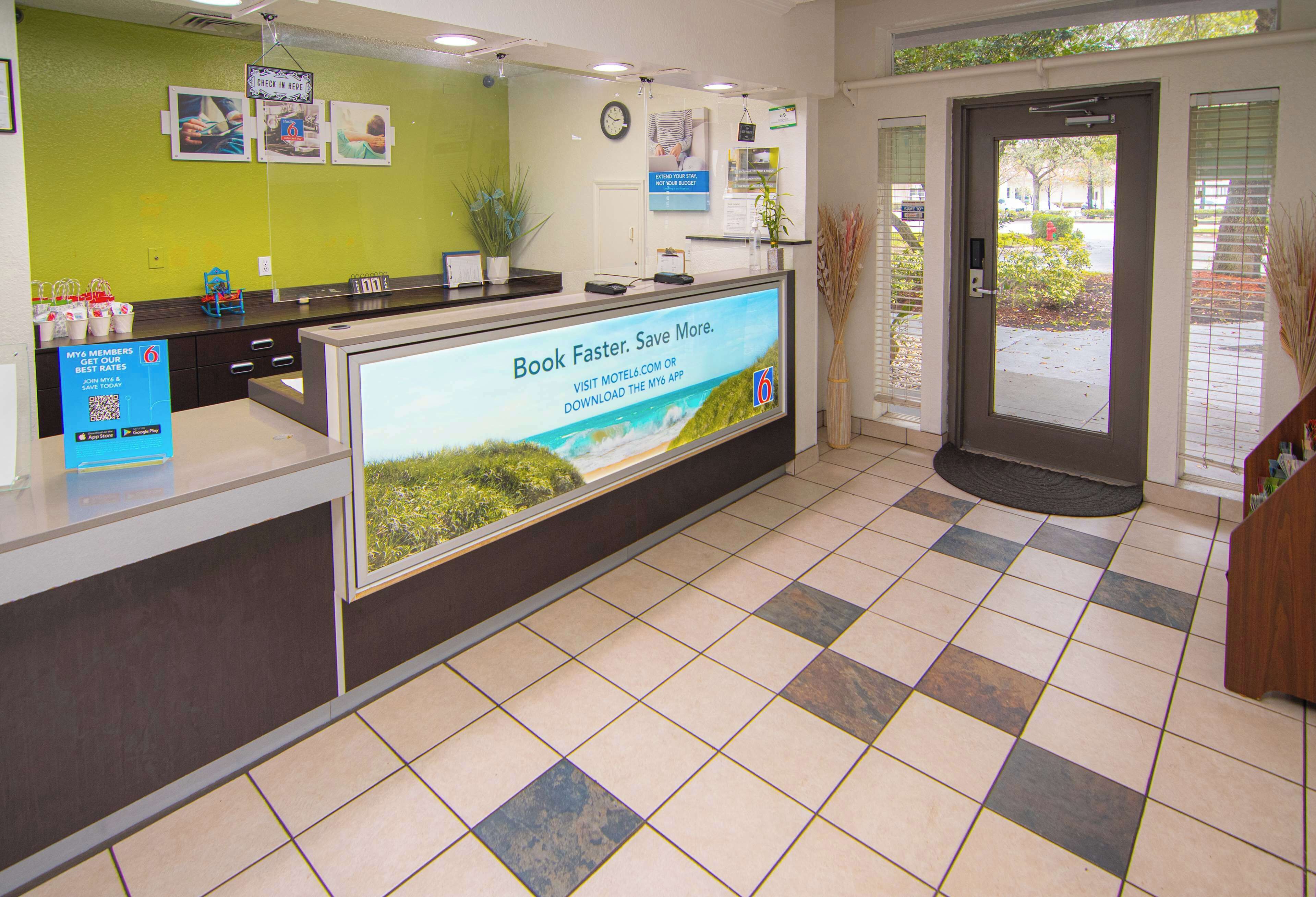 A reception area with a check-in counter, a digital screen displaying a message, and a door leading outside.