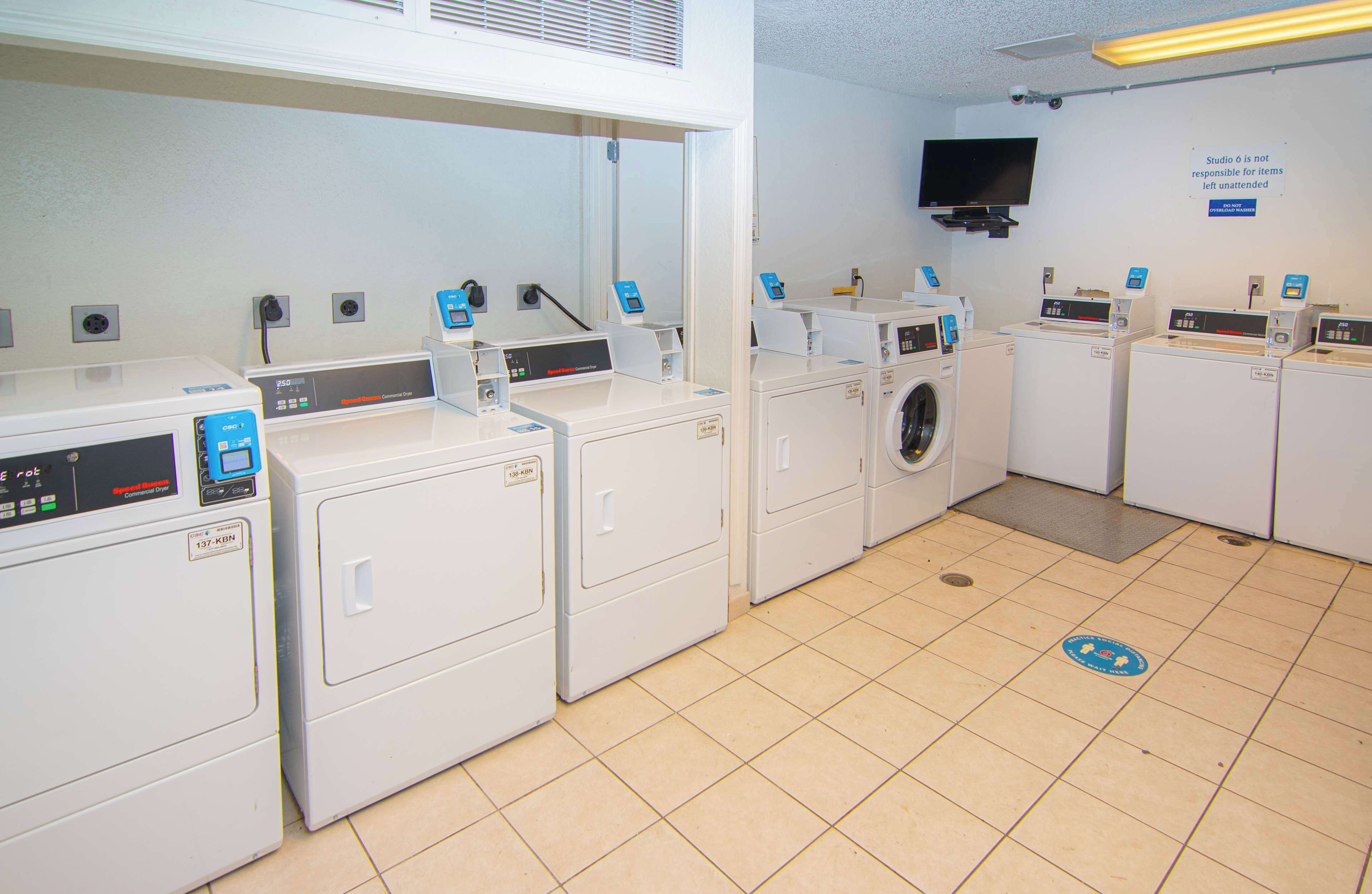 A laundry facility with multiple washing machines and dryers, a television mounted on the wall, and a sign indicating the location.