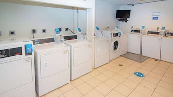 A laundry facility with multiple washing machines and dryers, a television mounted on the wall, and a sign indicating the location.