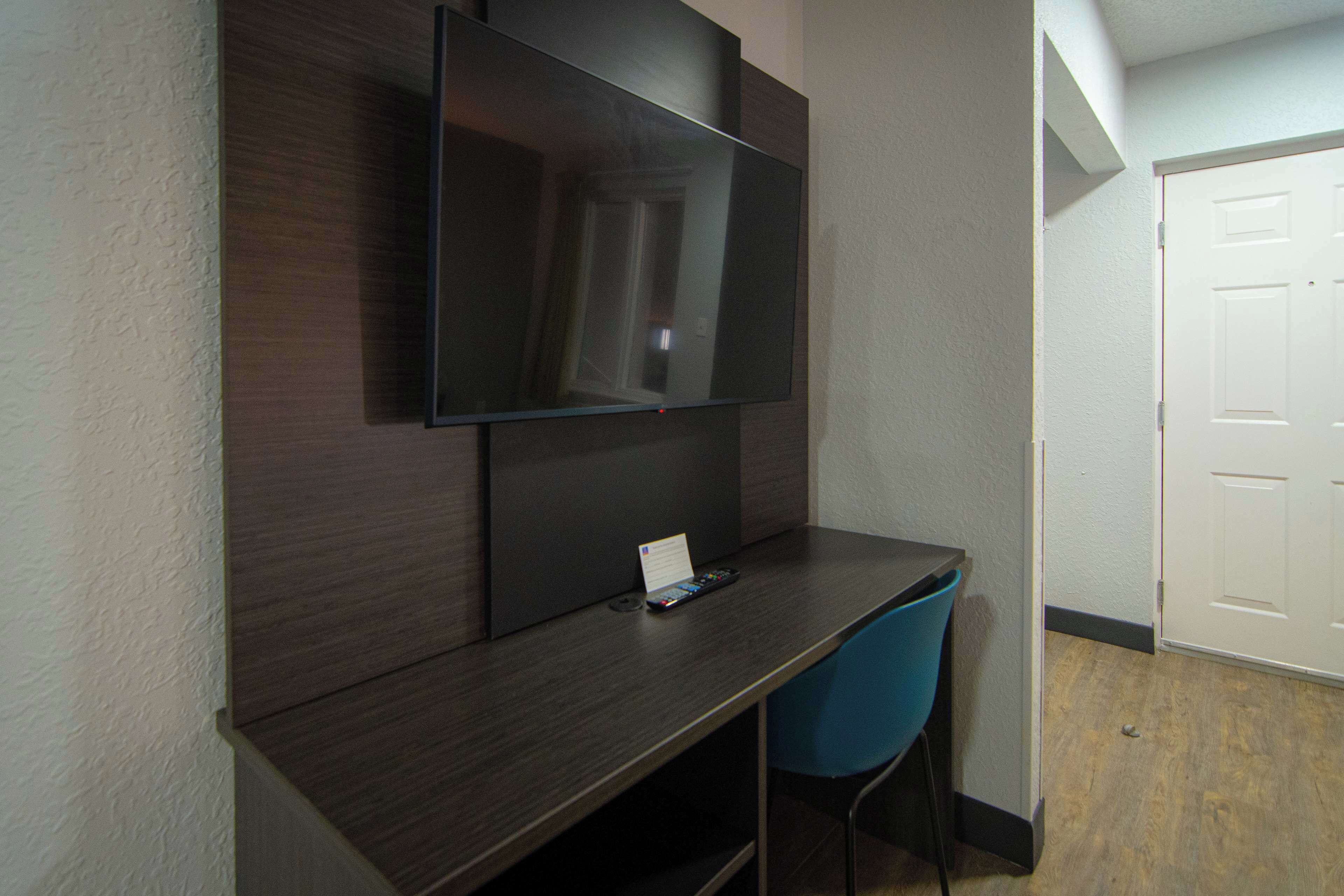 A dark wood desk with a flat-screen TV mounted above it, a small table, and a blue chair.