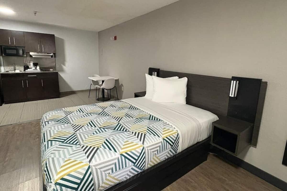 A hotel room with a bed, bedside tables, a desk, and a kitchenette.