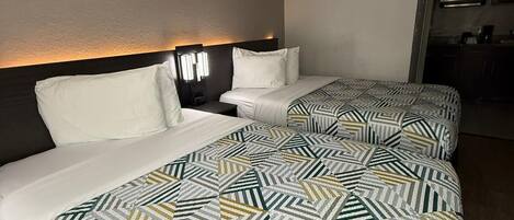 Una habitación de hotel con dos camas, cada una con una colcha estampada y almohadas blancas. Hay una mesita de noche con una lámpara entre las camas.