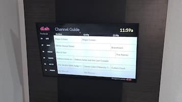 Habitació moderna amb televisió de pantalla plana penjada a una paret fosca, escriptori amb cadira i llit amb roba de llit a ratlles.
