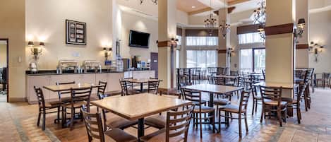 Un vaste espace dédié à la salle à manger, avec plusieurs tables et chaises, un coin cuisine équipé d’un espace pour préparer le café, et de grandes fenêtres laissant entrer la lumière naturelle.