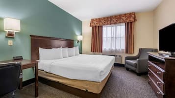 Habitación de hotel con una cama grande, un escritorio, una silla, un aparador, un televisor y una ventana con cortinas.