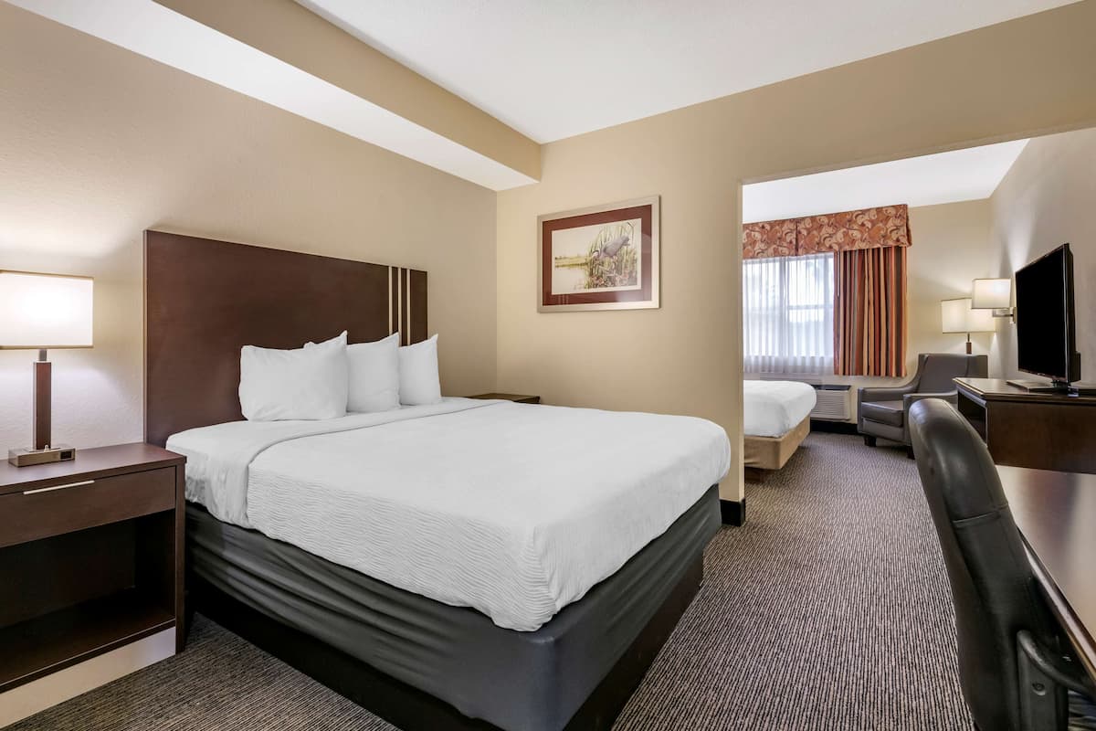 A hotel room with a large bed, a desk with a chair, a TV, and a window with curtains.