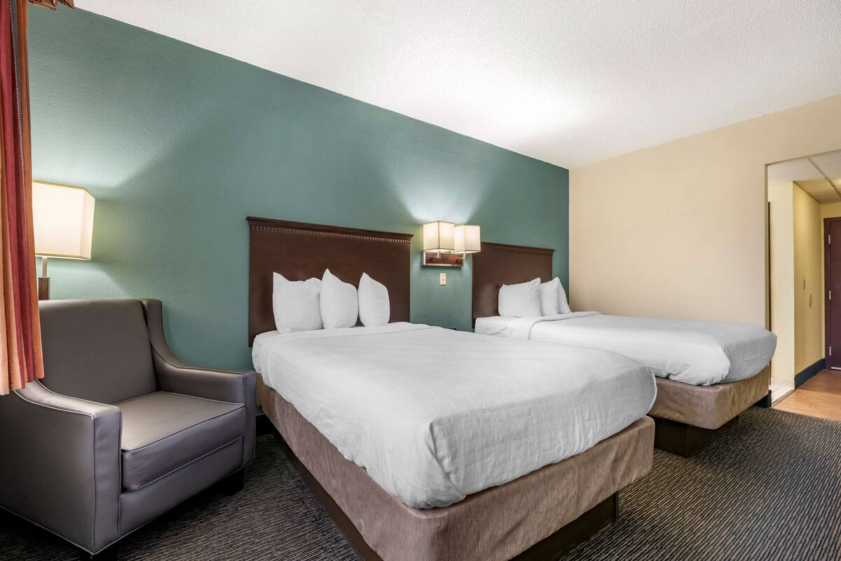 A hotel room with two beds, a chair, and a lamp.