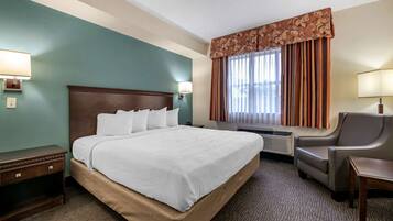 A hotel room with a large bed, a chair, a desk, and a window with curtains.