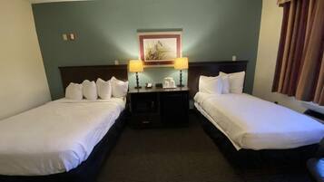 Habitación de hotel con dos camas individuales, una mesita de noche con lámpara, una pequeña mesa y un cuadro enmarcado en la pared.