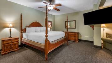 A four-poster bed with a ceiling fan, bedside tables with lamps, a flat-screen TV, and a green couch.