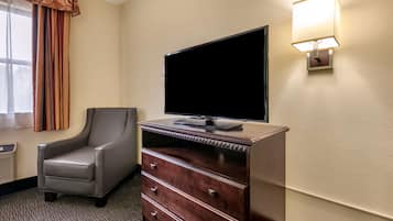Habitación de hotel con una televisión de pantalla plana sobre una cómoda de madera, un sillón de cuero y una lámpara de pared.