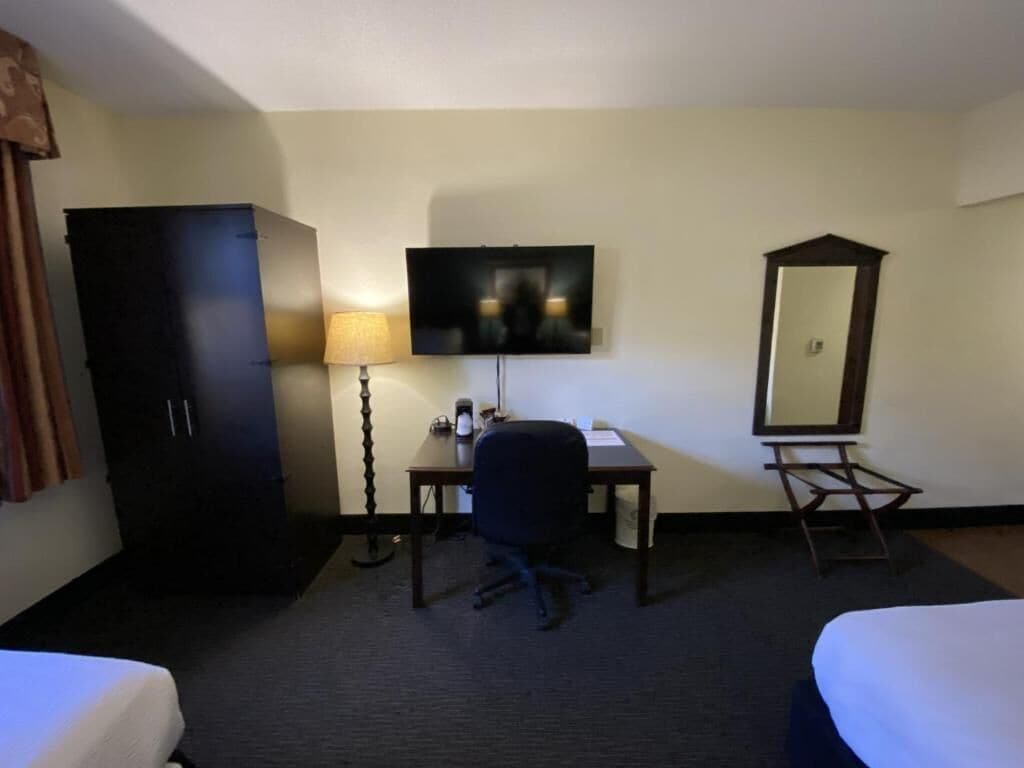 A hotel room with two beds, a desk with a chair, a TV, a mirror, and a wardrobe.