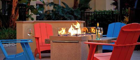 An outdoor seating area with a fire feature, red and blue chairs, and a table.