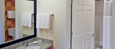 A bathroom with a granite countertop sink, a mirror, and a door leading to a shower.