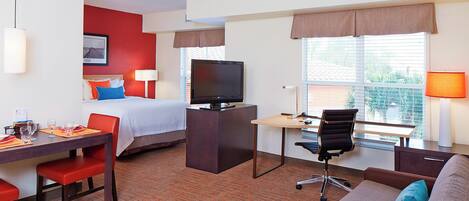 A hotel room with a bed, desk, chair, television, and a sofa.