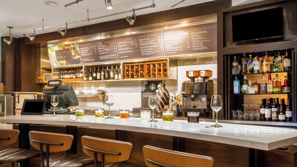Eine Bar mit einer langen Theke, Barhocker, einer Speisekarte und einer Auswahl an Flaschen und Gläsern.