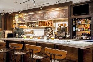 Un espace bar doté d’un long comptoir, de tabourets de bar, d’un tableau affichant le menu, ainsi que d’une variété de bouteilles et de verres.