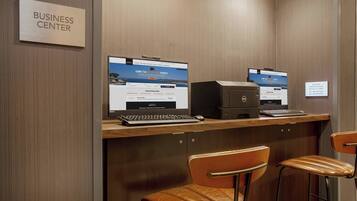 A business center with two computer workstations, a printer, and two leather chairs.